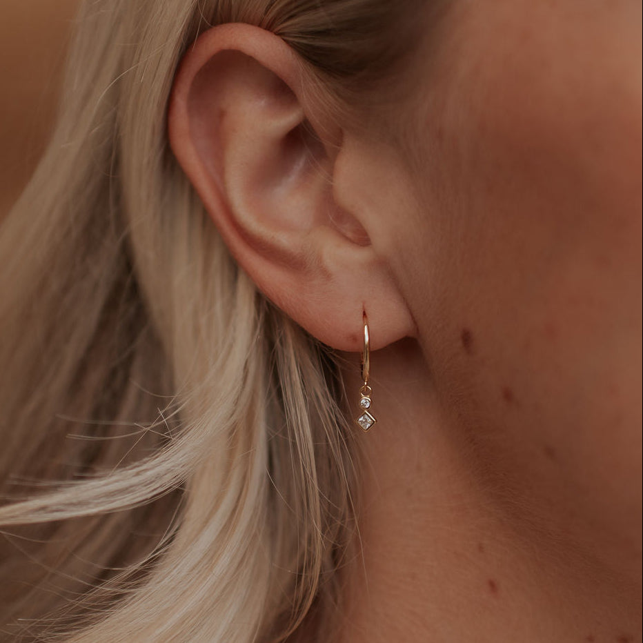 Close-up of an ear wearing a gold earring with a small gemstone.