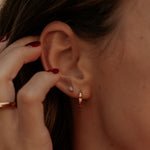 Close-up of an ear with earrings and a hand adjusting hair.