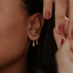 Load image into Gallery viewer, Close-up of a person wearing gold hoop earrings with a blurred background

