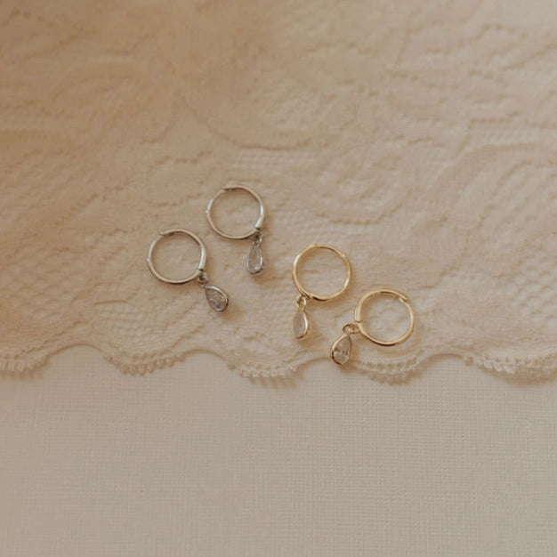 Gold and silver hoop earrings on a textured beige fabric background