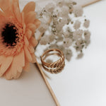 Gold ring on a white surface with a peach-colored flower and small white flowers.