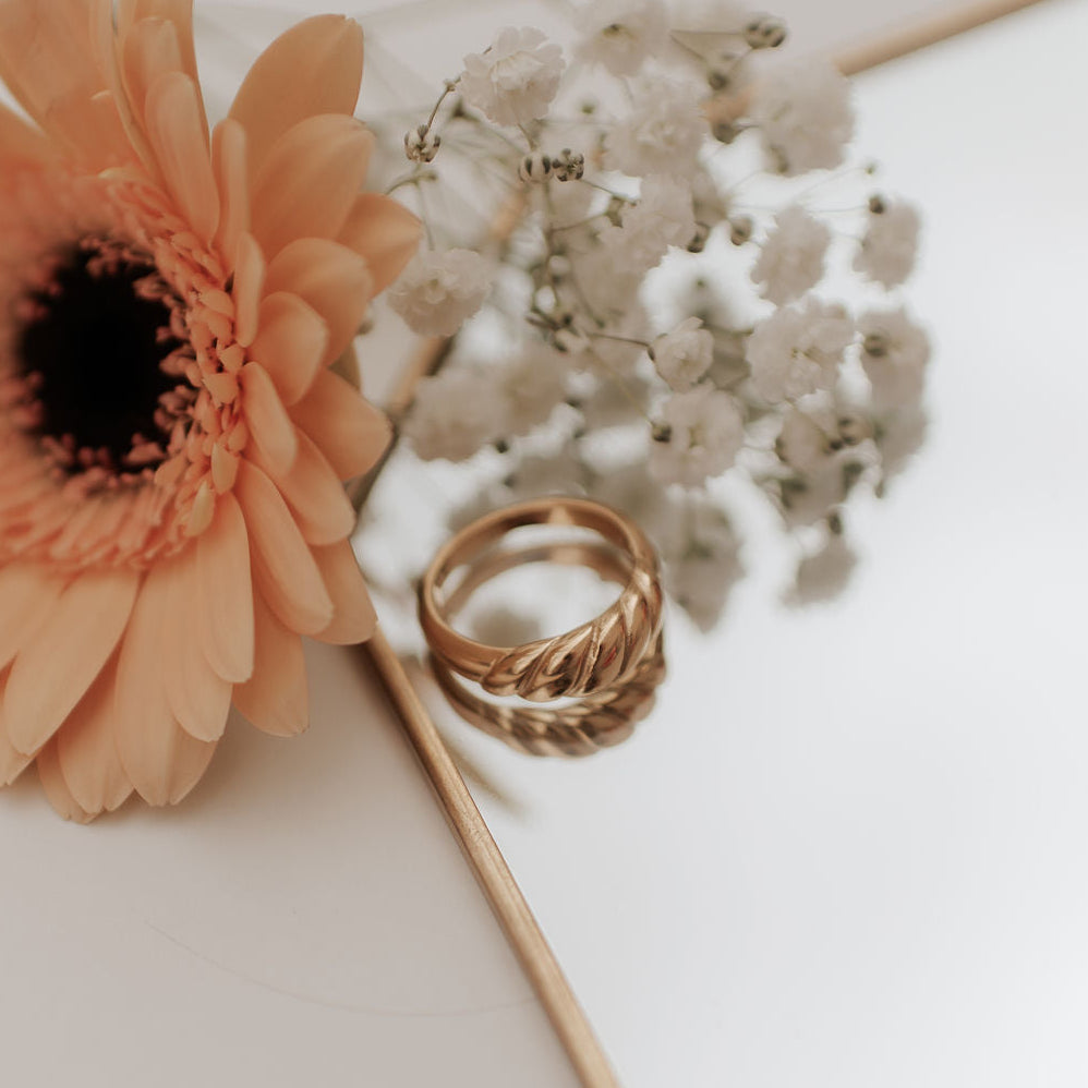 Gold ring on a white surface with a peach-colored flower and small white flowers.