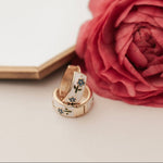 Load image into Gallery viewer, Two gold tea cup inspired earrings with gemstones on a white surface next to a pink rose.
