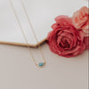 Necklace with a blue gemstone on a white surface with pink flowers.