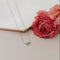 Necklace with a blue gemstone on a white surface with pink flowers.
