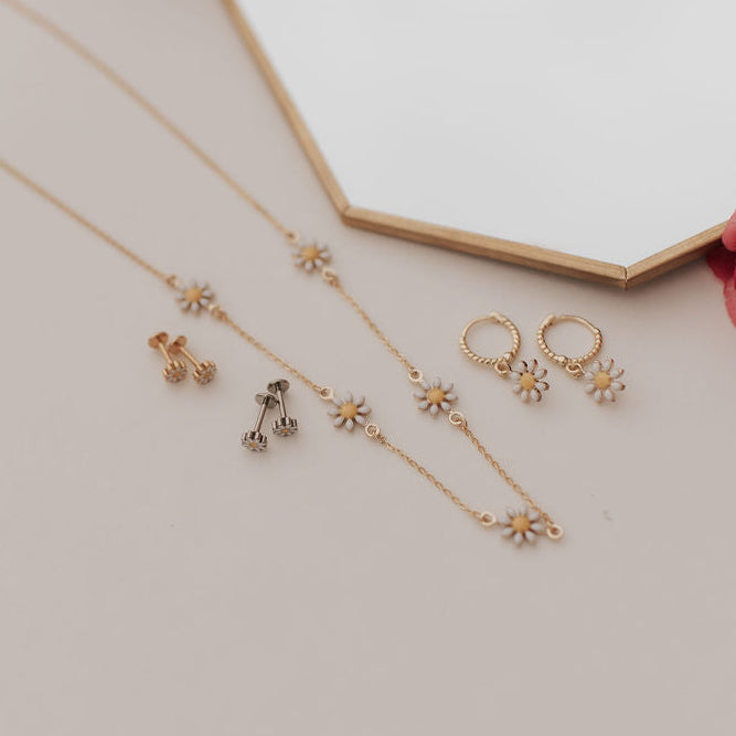 Gold jewelry set with necklace and earrings on a light surface with a pink rose.
