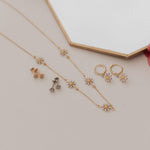 Gold jewelry set with necklace and earrings on a light surface with a pink rose.