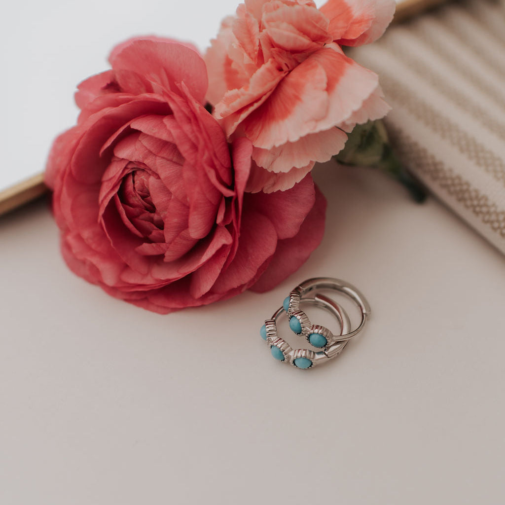 Two pink flowers with a silver earrings featuring turquoise stones on a light surface.