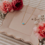 Gold necklace with a turquoise pendant on a decorative plate with flowers