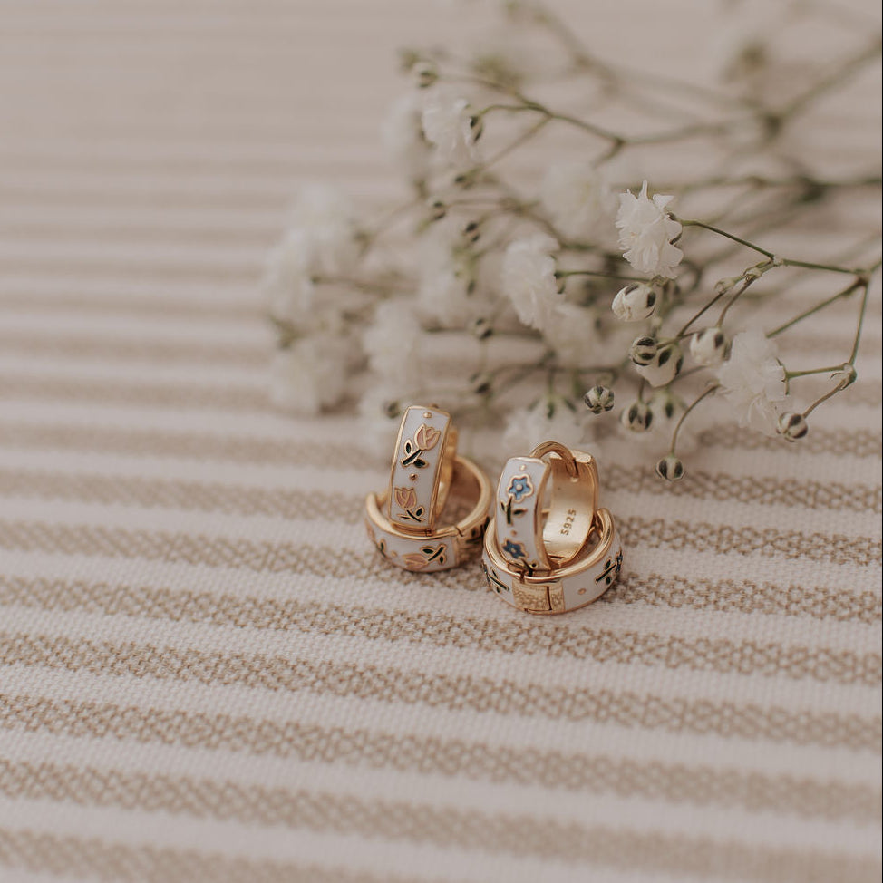 Pair of gold earrings on a striped fabric background with small white flowers.