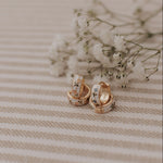 Load image into Gallery viewer, Pair of gold earrings on a striped fabric background with small white flowers.
