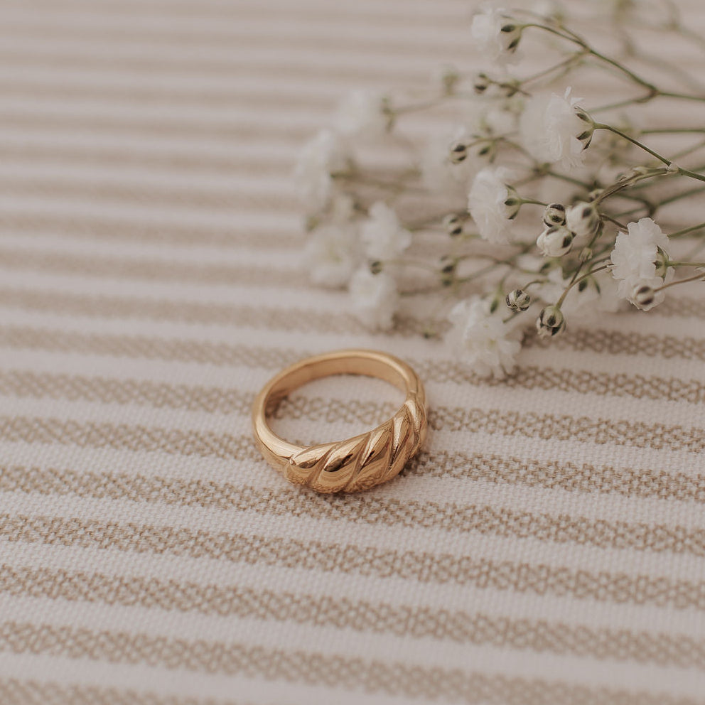 Gold ring on a beige striped fabric background with small white flowers.