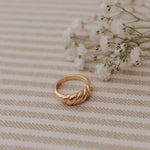 Load image into Gallery viewer, Gold ring on a beige striped fabric background with small white flowers.
