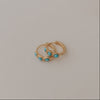 Two gold earrings with turquoise stones on a light gray background