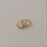 Two gold earrings with turquoise stones on a light gray background