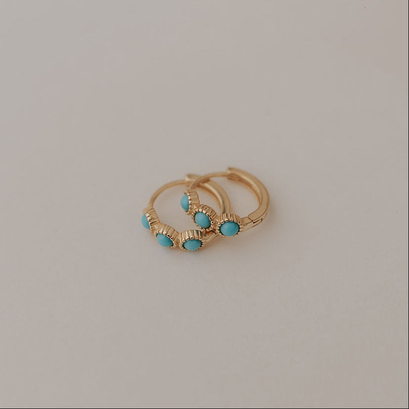 Two gold earrings with turquoise stones on a light gray background