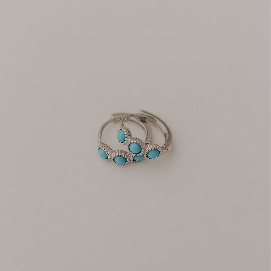Silver earrings with turquoise stones on a light gray background