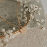 Gold necklace with a round pendant on a textured surface with small white flowers.