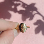 Gold ring with floral design held by a hand on a pink background