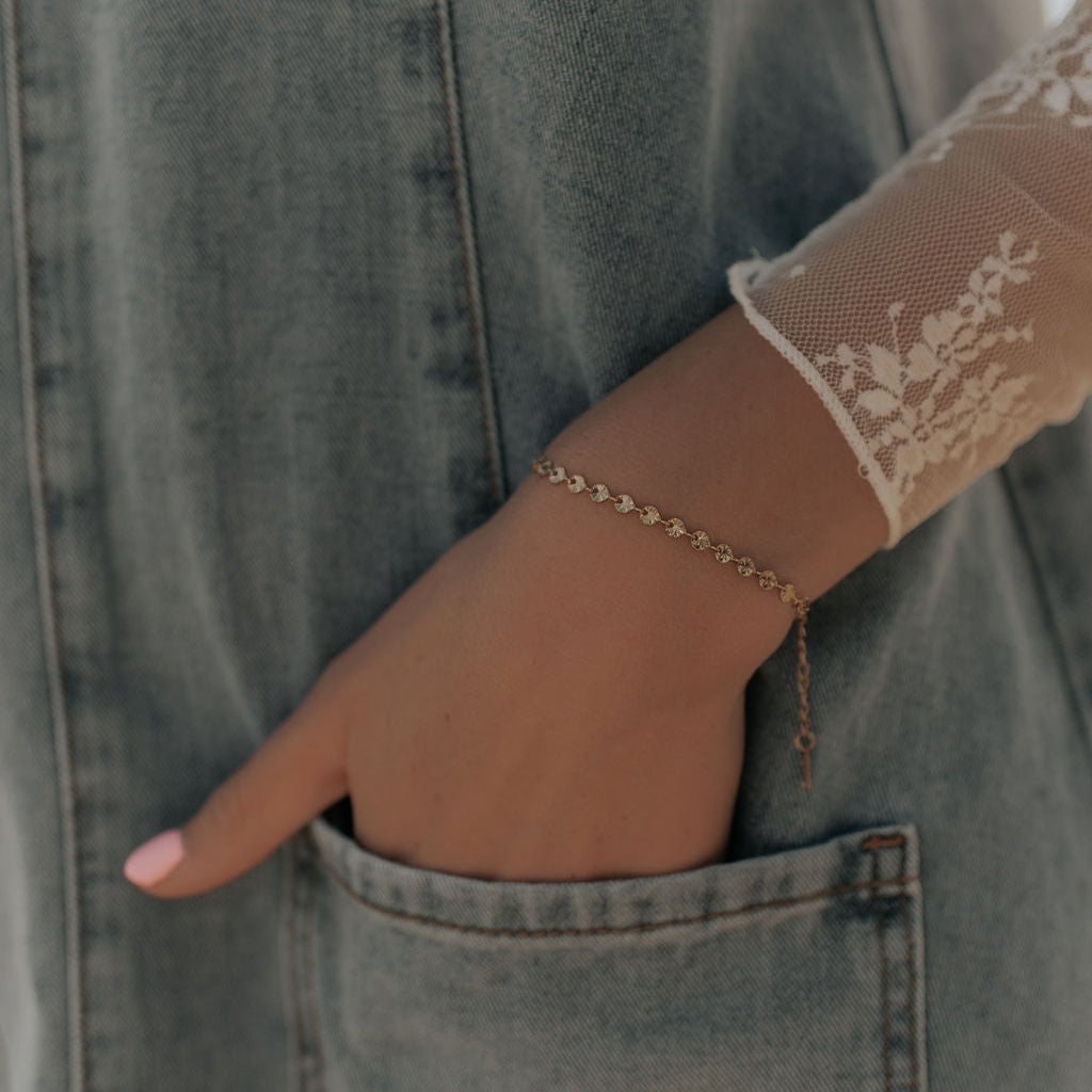 Hand with a gold bracelet resting on a denim surface