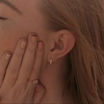 Close-up of a person wearing gold earrings and rings with a blurred background