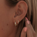 Close-up of an ear with gold star hoop earrings and a hand touching the earlobe.