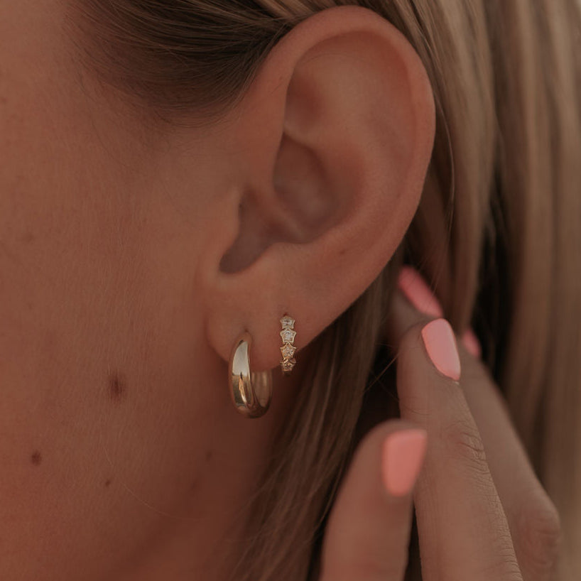 Close-up of an ear with gold star hoop earrings and a hand touching the earlobe.