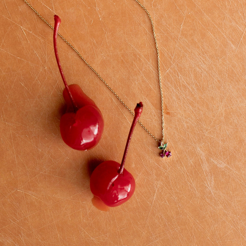 Two red cherries on a gold chain against a beige background