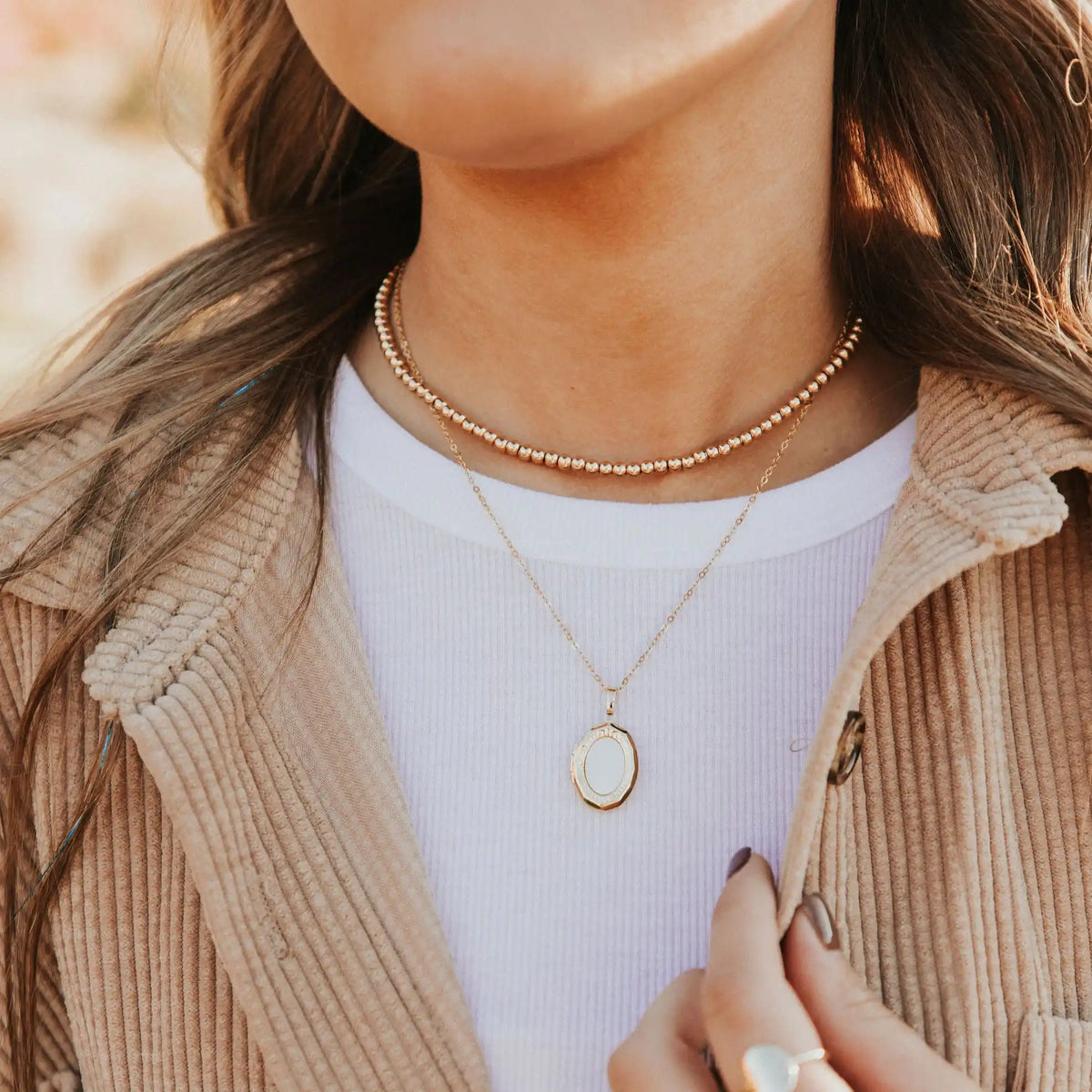 Person wearing two gold necklaces with a blurred background