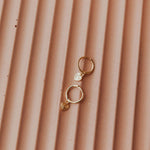 Gold hoop earrings with heart charms on a textured brown surface