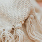 Close-up of beige knitted fabric with a gold earring on a blurred background