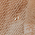 Small cross-shaped earrings on a textured beige fabric background