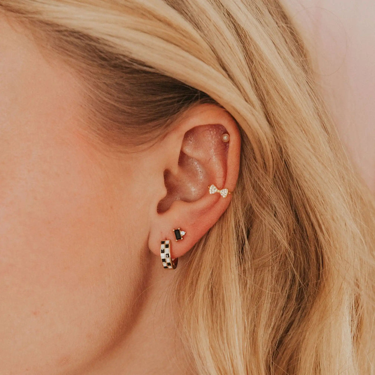 Close-up of an ear wearing multiple earrings with a neutral background