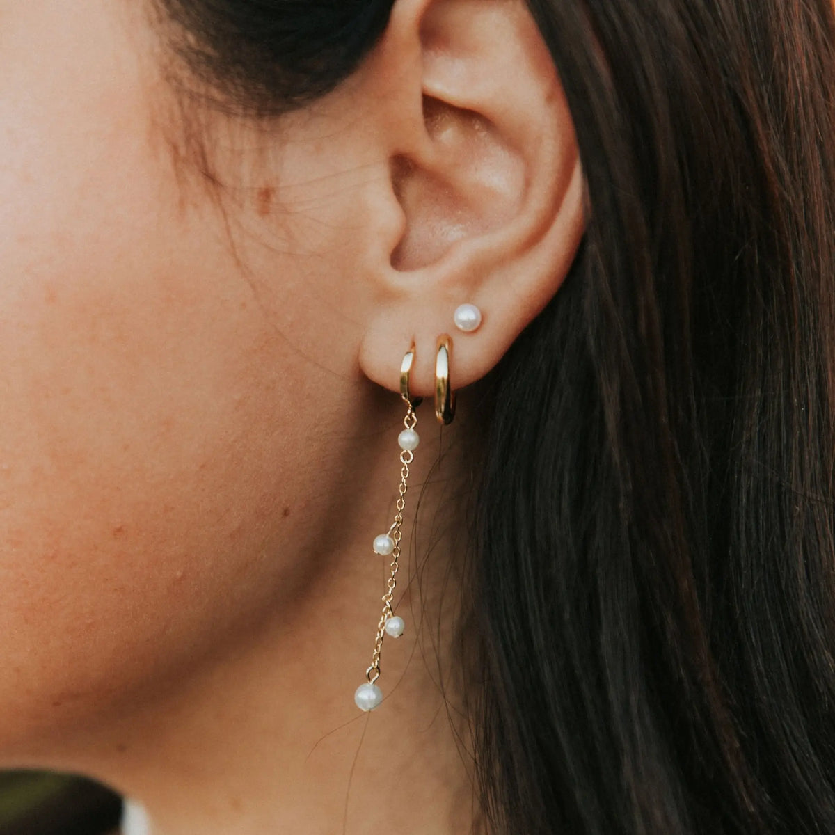 Close-up of an ear wearing gold hoop earrings with pearl drop earrings.