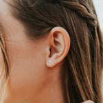 Close-up of an ear with a pearl earring, hair styled in braids.