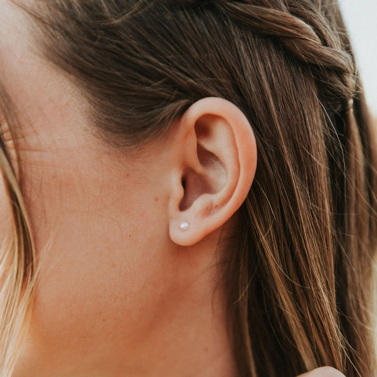 Close-up of an ear with a pearl earring, hair styled in braids.