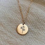 Load image into Gallery viewer, Gold necklace with a round pendant featuring a floral design on a beige fabric background
