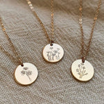 Load image into Gallery viewer, Three gold necklaces with circular pendants featuring floral designs on a textured beige fabric background.
