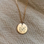 Gold necklace with a round pendant featuring floral designs on a textured beige fabric background