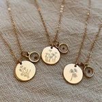 Three gold necklaces with circular pendants featuring floral designs on a textured fabric background.