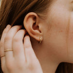 A close-up image of a woman's ear wearing a gold hoop earring.
