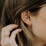 A person wearing gold hoop earrings with a twist design.