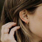 A person wearing gold hoop earrings with a twist design.